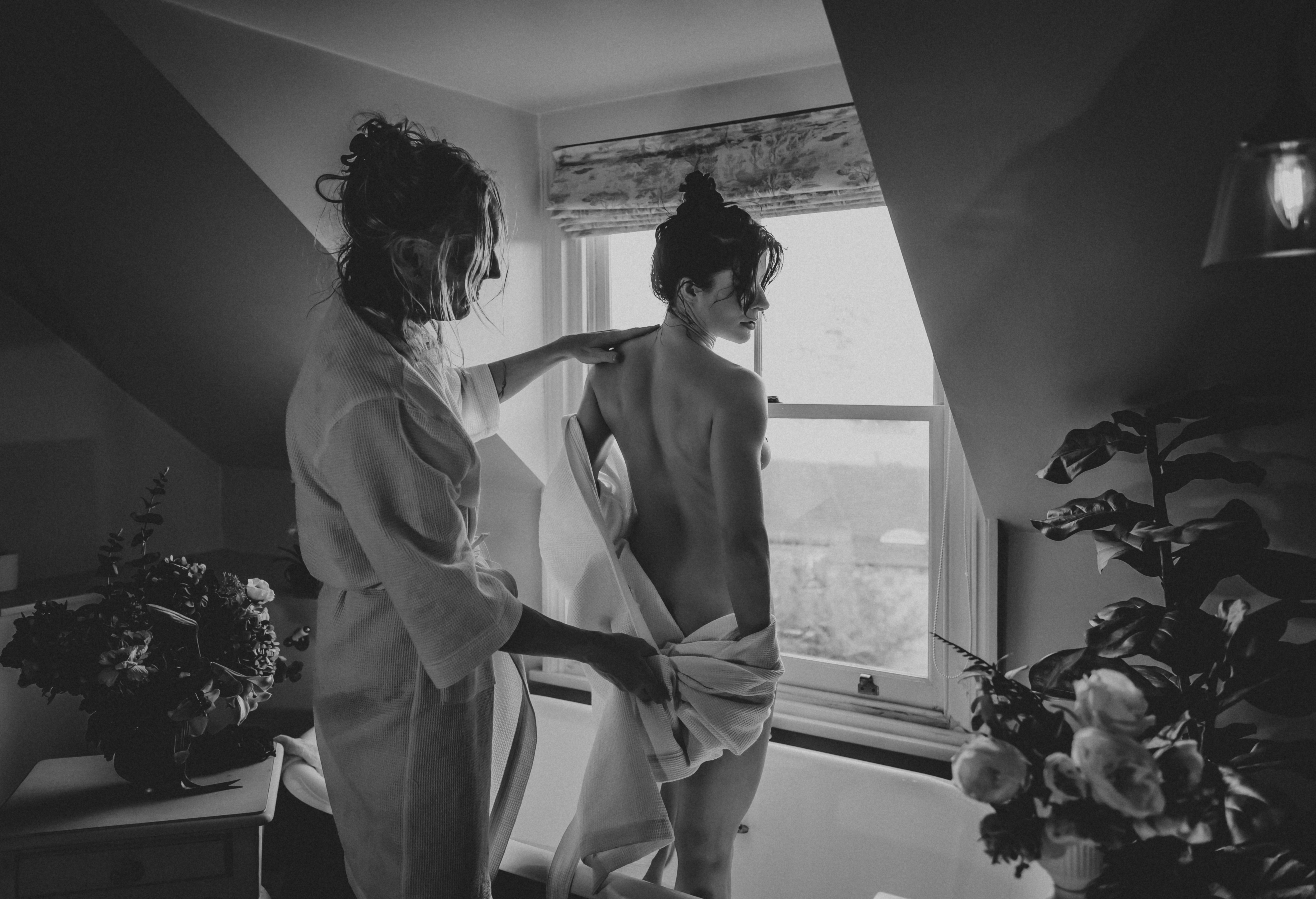 Black and white photo of two people near a window, one gently touching the other’s back, showing calm connection and trust.